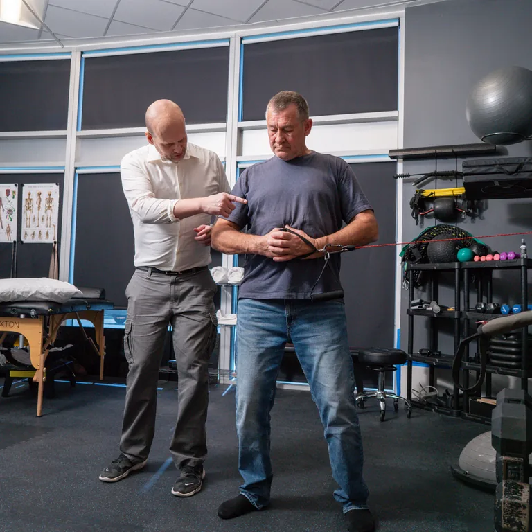 Dr. Edward Shut guiding a man through a standing resistance-band exercise at Chatsworth Physical Therapy.